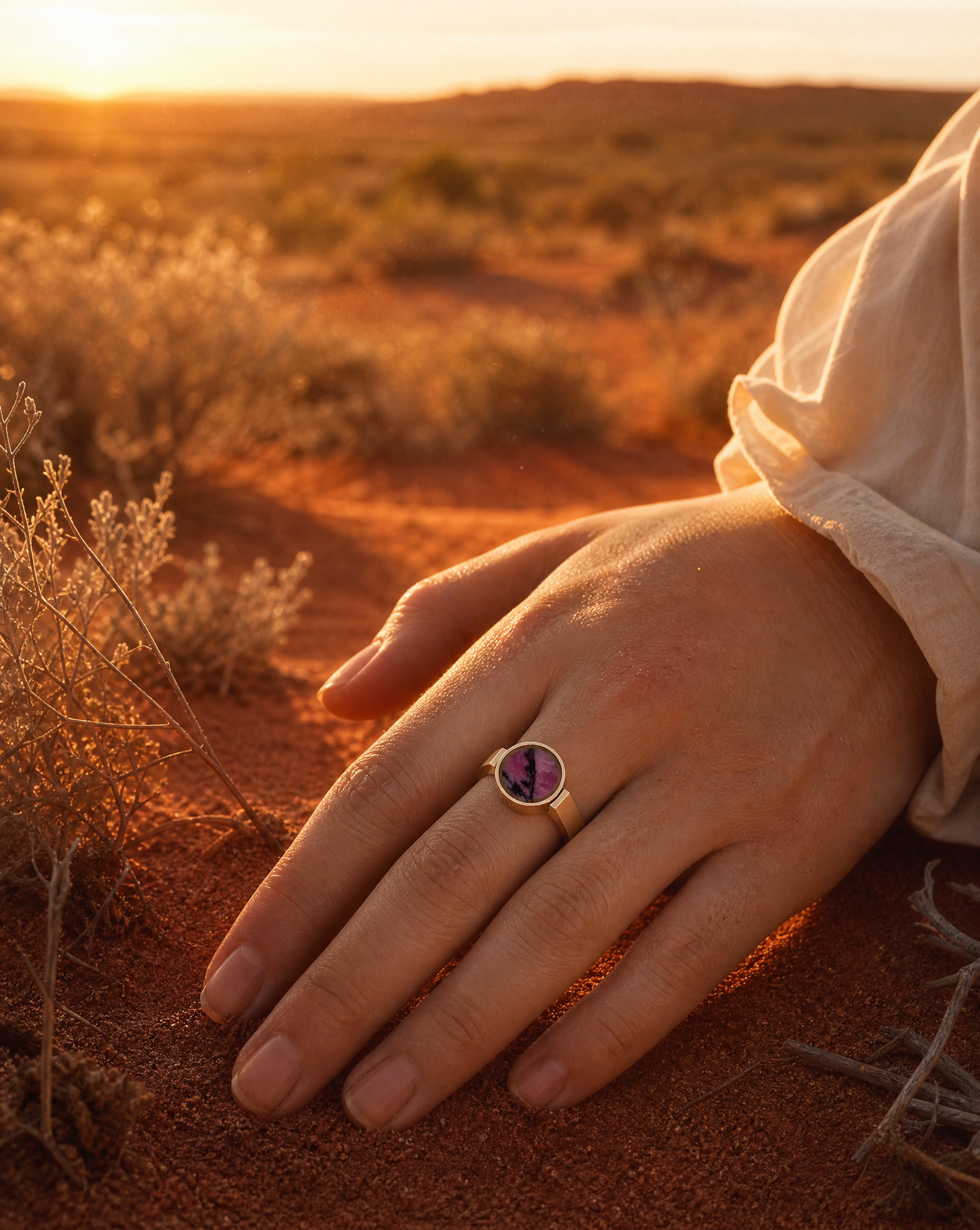 Australian rhodonite unisex ring worn on a hand against red desert sand dunes at golden hour