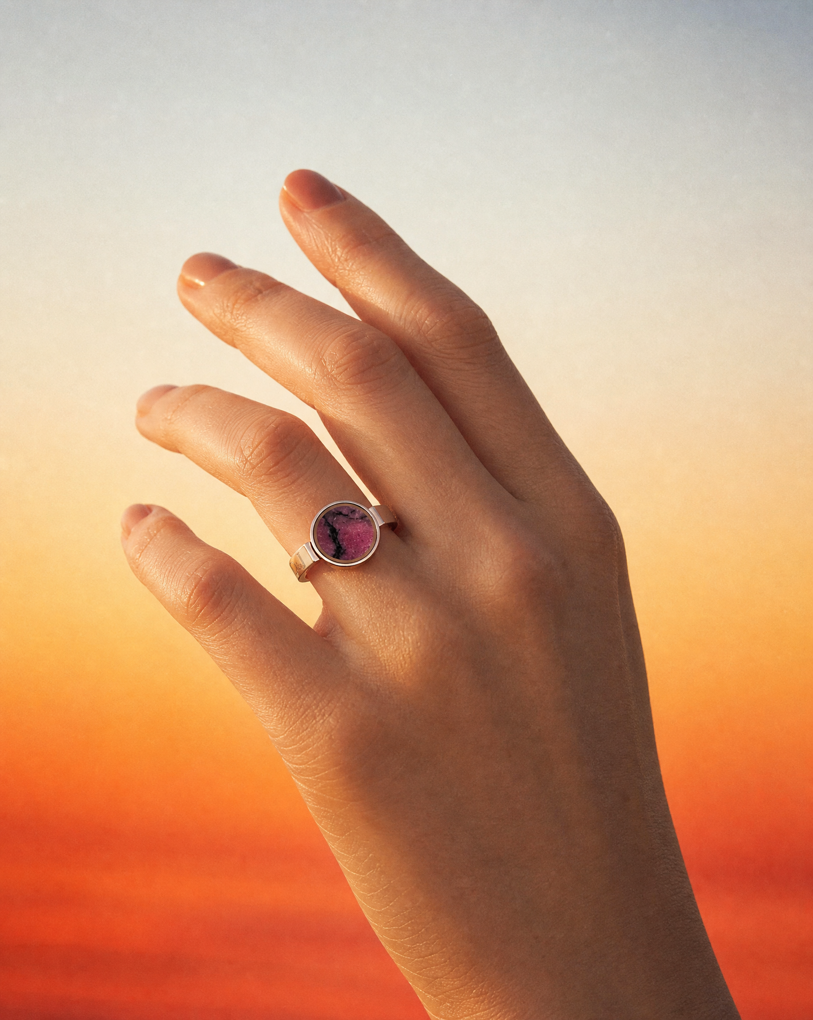 Close up of the Australian rhodonite unisex ring on a raised hand against a warm sunset gradient
