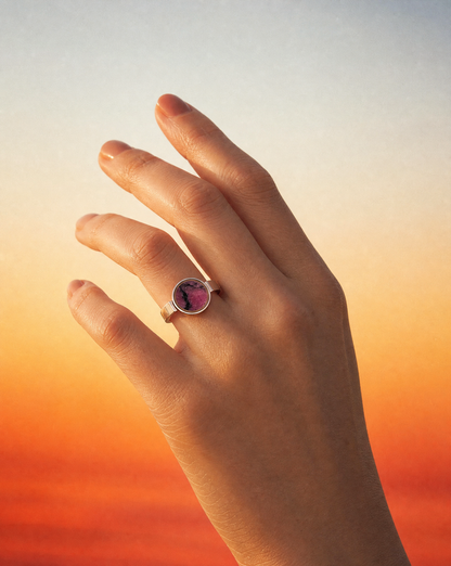Close up of the Australian rhodonite unisex ring on a raised hand against a warm sunset gradient