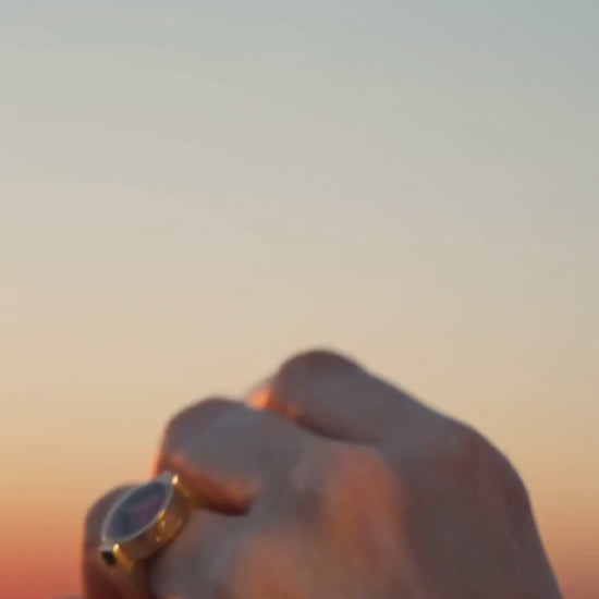 Australian rhodonite unisex ring on a hand against a sunset gradient background