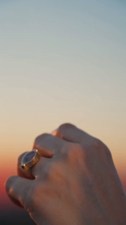 Australian rhodonite unisex ring on a hand against a sunset gradient background