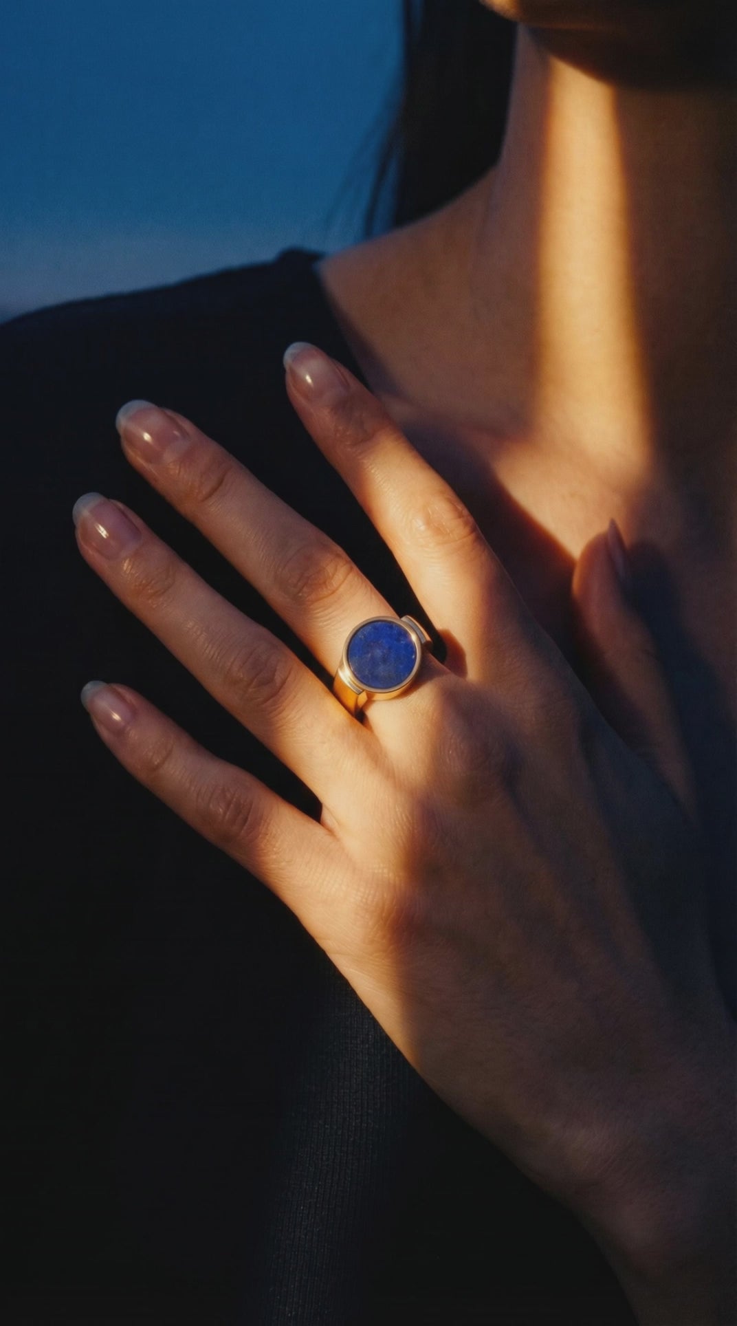 Lapis lazuli unisex signet ring worn on a hand resting at the collarbone in warm dusk light