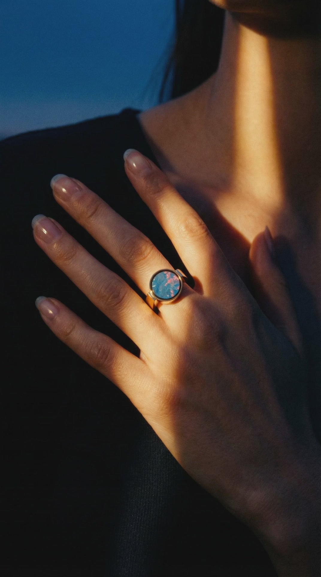 Australian opal unisex signet ring worn on a hand resting at the collarbone in warm dusk light