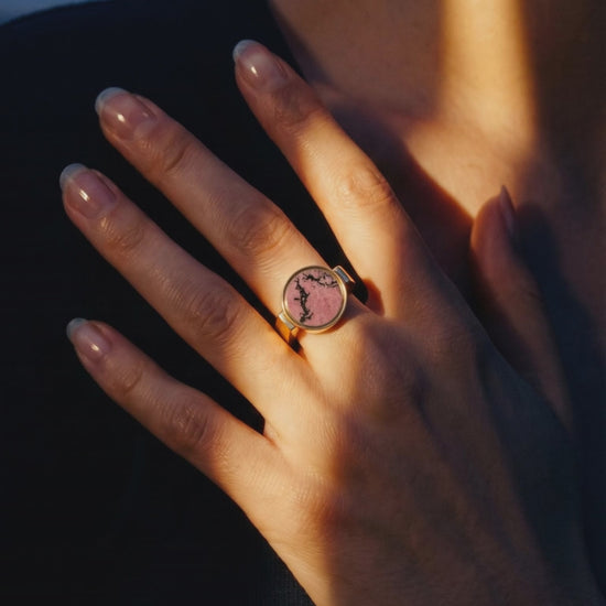 Australian rhodonite unisex signet ring worn on a hand resting at the collarbone in warm dusk light