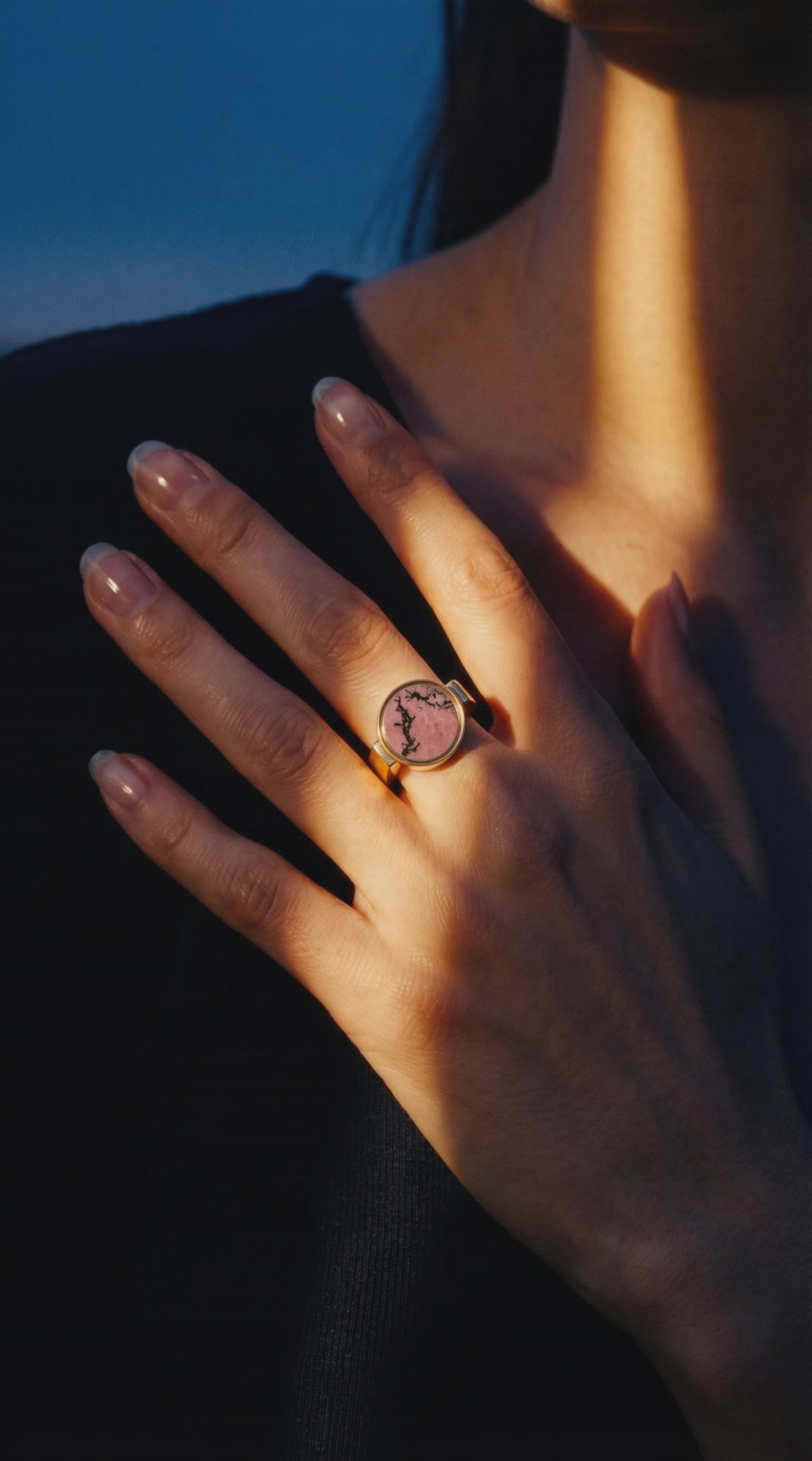 Australian rhodonite unisex signet ring worn on a hand resting at the collarbone in warm dusk light